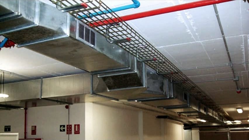 Conductos de ventilación de chapa galvanizada con rejillas de impulsión bajo el forjado de un aparcamiento en Madrid