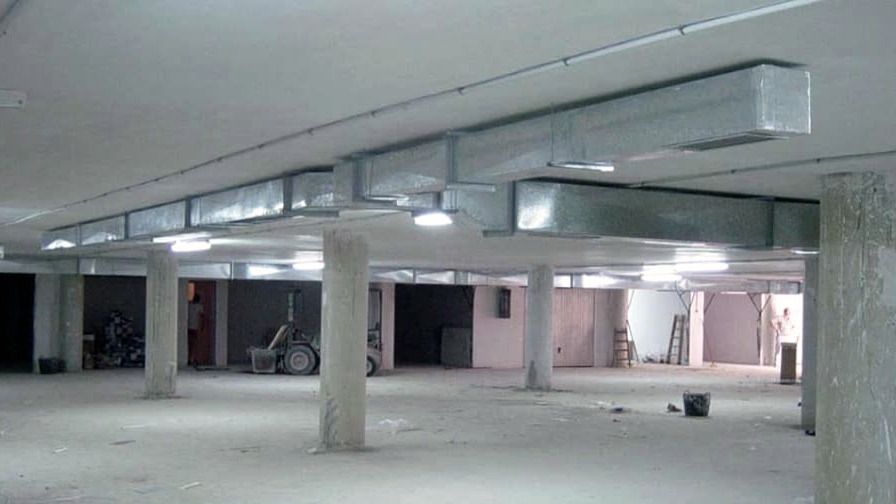 Conductos de ventilación rectangulares suspendidos con varilla roscada bajo el forjado de un sótano en obra